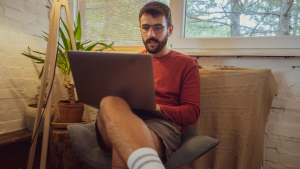 Homem trabalhando em casa com seu computador no colo.